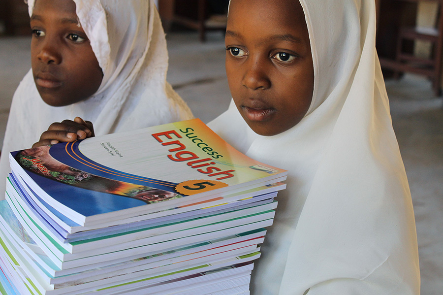 Schüler der Mkuti-Grundschule halten Bücher, ein von African Palms finanziertes Projekt verkaufen Palmkreuze
